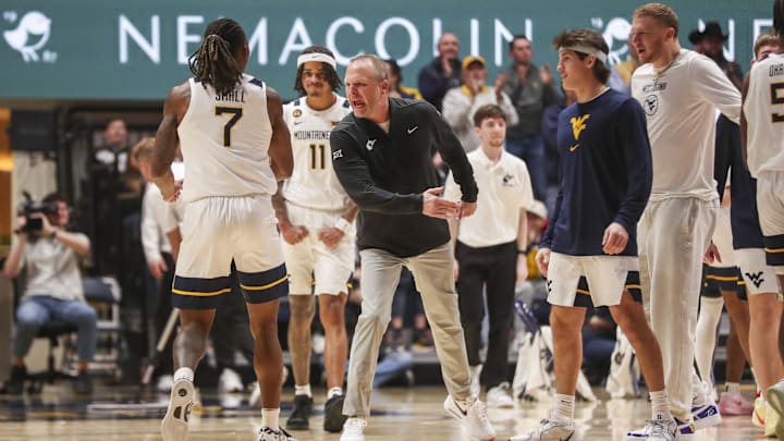 Jan 4, 2025; Morgantown, West Virginia, USA; West Virginia Mountaineers head coach Darian DeVries celebrates with West Virginia Mountaineers guard Javon Small (7) during the first half against the Oklahoma State Cowboys at WVU Coliseum. Mandatory Credit: Ben Queen-Imagn Images