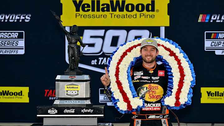 Chase Briscoe poses next to the trophy while wearing the customary winner's floral wreath in victory lane following a win in the YellaWood 500 at Talladega Superspeedway.