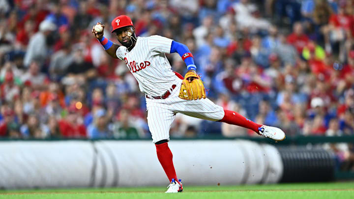 Philadelphia Phillies infielder Rodolfo Castro throws across his body, wearing a white and red pinstripe jersey and a red hat
