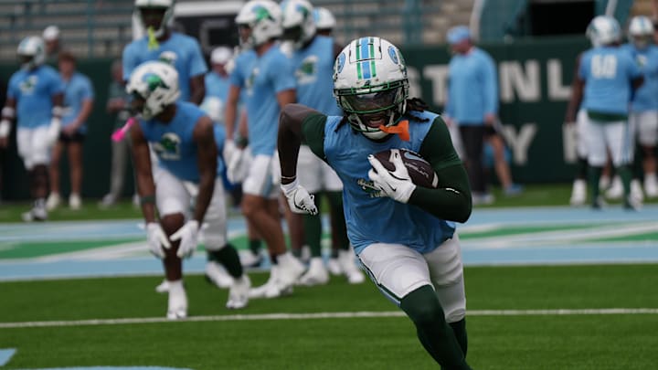 A Tulane Green Wave football player runs in practice with the ball in his hands
