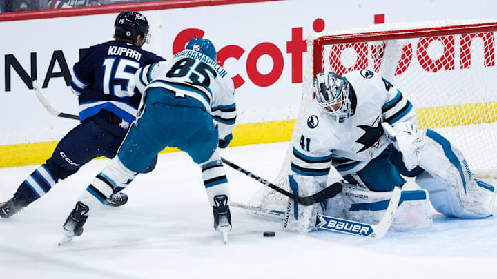 Feb 24, 2025; Winnipeg, Manitoba, CAN;  San Jose Sharks defenseman Shakir Muhamadullin (85) checks Winnipeg Jets forward Rasmus Kupari (15) in front of San Jose Sharks goalie Vitek Vanecek (41) during the third period at Canada Life Centre. Mandatory Credit: Terrence Lee-Imagn Images