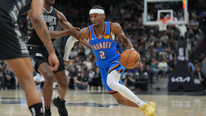 Mar 2, 2025; San Antonio, Texas, USA; Oklahoma City Thunder guard Shai Gilgeous-Alexander (2) dribbles past San Antonio Spurs center Bismack Biyombo (18) in the second half at Frost Bank Center. Mandatory Credit: Daniel Dunn-Imagn Images Mar 2, 2025; San Antonio, Texas, USA; Oklahoma City Thunder guard Shai Gilgeous-Alexander (2) dribbles past San Antonio Spurs center Bismack Biyombo (18) in the second half at Frost Bank Center. Mandatory Credit: Daniel Dunn-Imagn Images