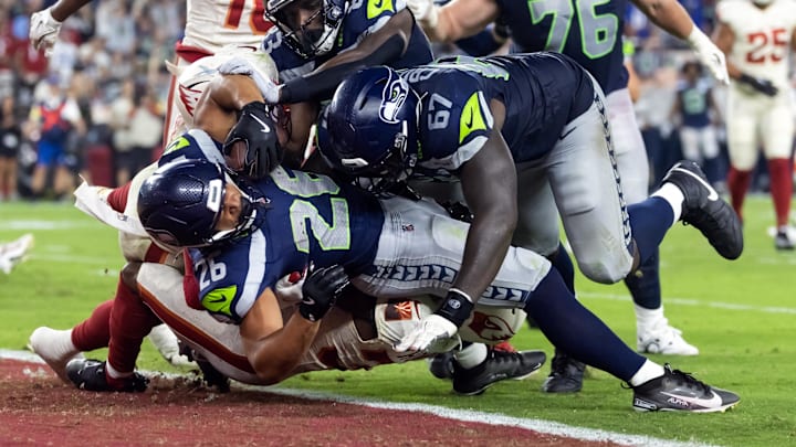 Sep 25, 2025; Glendale, Arizona, USA; Seattle Seahawks running back Zach Charbonnet (26) is pushed across the goal line by tackle Charles Cross (67) to score a touchdown against Arizona Cardinals safety Jalen Thompson (34) in the second quarter at State Farm Stadium. Mandatory Credit: Mark J. Rebilas-Imagn Images
