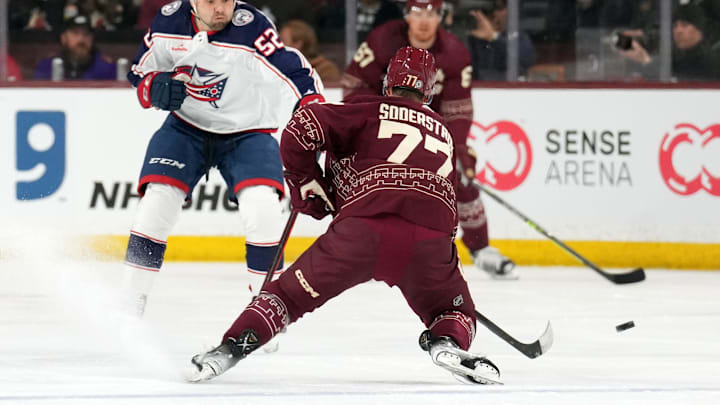 Feb 19, 2023; Tempe, Arizona, USA; Arizona Coyotes defenseman Victor Soderstrom (77) moves the puck by Columbus Blue Jackets right wing Emil Bemstrom (52) during the first period at Mullett Arena. Mandatory Credit: Joe Camporeale-Imagn Images
