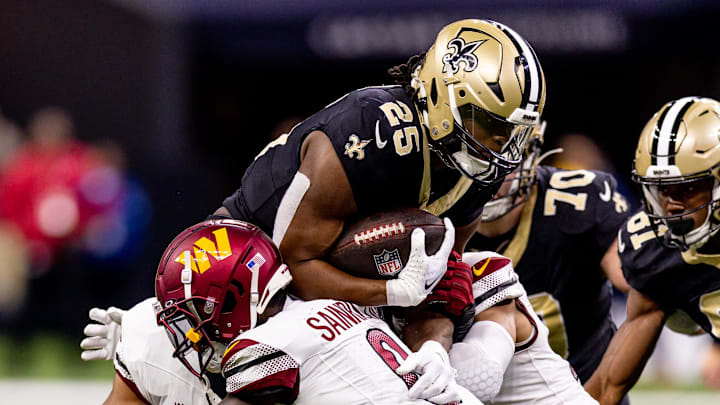 Dec 15, 2024; New Orleans, Louisiana, USA;  New Orleans Saints running back Kendre Miller (25)  is tackled by Washington Commanders cornerback Mike Sainristil (0) during the second half at Caesars Superdome. Mandatory Credit: Stephen Lew-Imagn Images