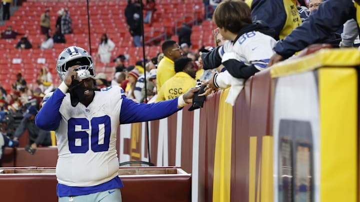 Dallas Cowboys offensive tackle Tyler Guyton hands his glove to a young fan while leaving the field after a game.