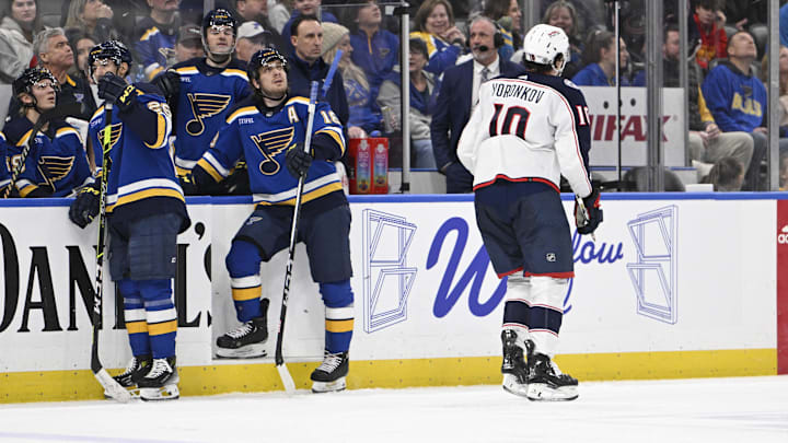 St Louis Blues forwards Jordan Kyrou and Robert Thomas stand by the bench as Blue Jackets forward Dmitri Voronkov skates by.
