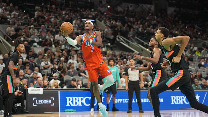 Dec 23, 2025; San Antonio, Texas, USA; Oklahoma City Thunder guard Shai Gilgeous-Alexander (2) drives to the basket between San Antonio Spurs forward Victor Wembanyama (1) and guard Stephon Castle (5) during the second half at Frost Bank Center. Mandatory Credit: Scott Wachter-Imagn Images