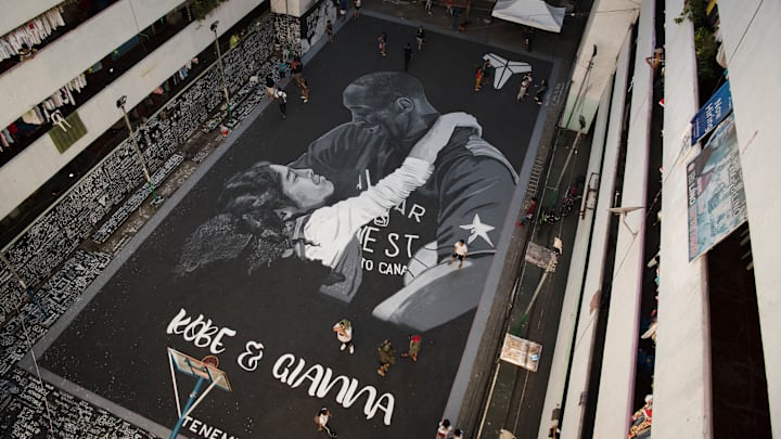 People walk beside a giant mural of Kobe and Gianna Bryant...