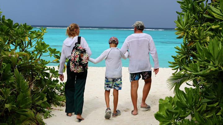 A family with a child walks along the white sandy beach on...
