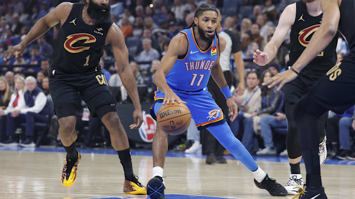 Feb 22, 2026; Oklahoma City, Oklahoma, USA; Oklahoma City Thunder guard Isaiah Joe (11) drives between Cleveland Cavaliers guard James Harden (1) and Cleveland Cavaliers forward Dean Wade (32) during the first half at Paycom Center.