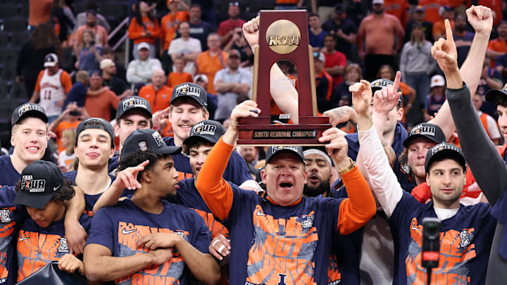 Mar 28, 2026; Houston, TX, USA; Illinois Fighting Illini head coach Brad Underwood and players celebrate with the trophy on the podium after defeating the Iowa Hawkeyes in an Elite Eight game of the South Regional of the men's 2026 NCAA Tournament at Toyota Center. Mandatory Credit: Troy Taormina-Imagn Images