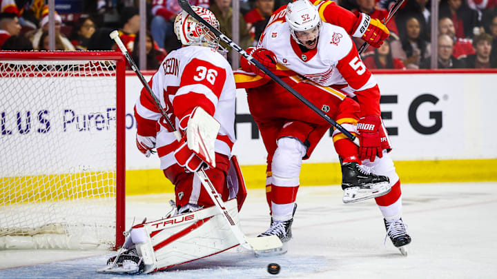 Dec 10, 2025; Calgary, Alberta, CAN; Detroit Red Wings defenseman Travis Hamonic (52) and Calgary Flames right wing Matt Coronato (27) fight for position in front of Detroit Red Wings goaltender John Gibson (36) during the second period at Scotiabank Saddledome. Mandatory Credit: Sergei Belski-Imagn Images