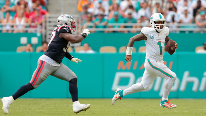 Sep 14, 2025; Miami Gardens, Florida, USA; Miami Dolphins quarterback Tua Tagovailoa (1) carries the football against New England Patriots defensive end Milton Williams (97) during the fourth quarter at Hard Rock Stadium. Mandatory Credit: Sam Navarro-Imagn Images