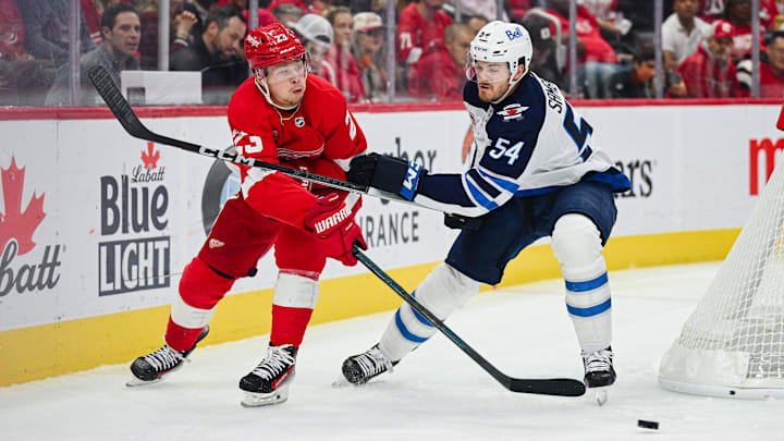 Oct 30, 2024; Detroit, Michigan, USA; Detroit Red Wings left wing Lucas Raymond (23) passes the puck as Winnipeg Jets defenseman Dylan Samberg (54) defends during the second period at Little Caesars Arena. Mandatory Credit: Tim Fuller-Imagn Images