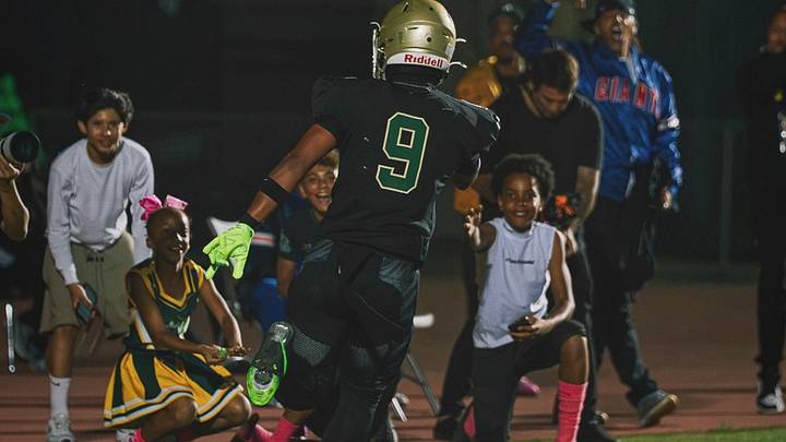 As a Long Beach Poly's Jeron Johnson II makes his way toward the end zone, Pop Warner players, cheerleaders and fans line the sidelines, capturing the community spirit and tradition