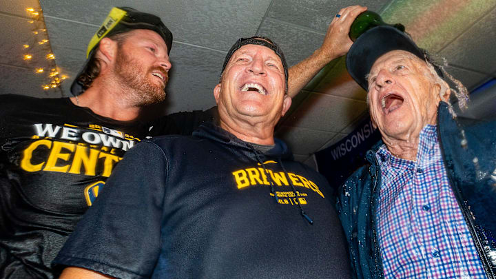 Milwaukee pitcher Brandon Woodruff pours champagne over  broadcaster Bob Uecker and manager Pat Murphy after winning the NL Central Division title.