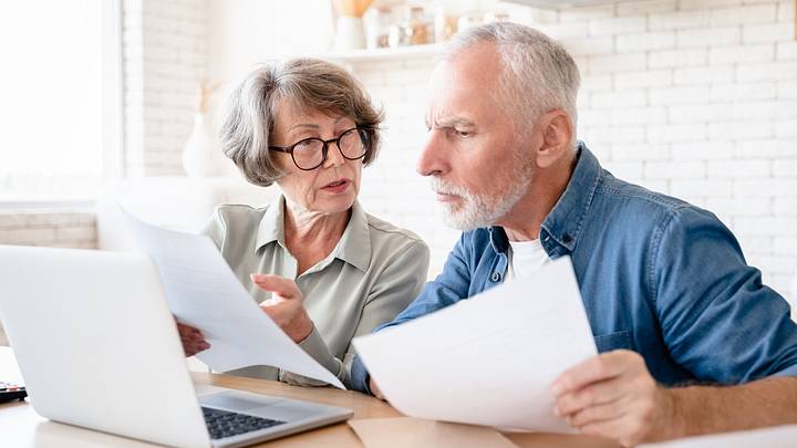 Older couple at table looking at sheets and computer 