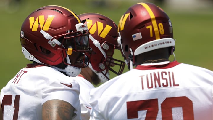 Washington Commanders offensive linemen stand on the field between drills on day one of minicamp.