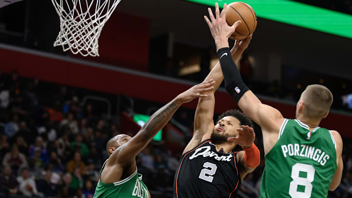Mar 22, 2024; Detroit, Michigan, USA; Detroit Pistons guard Cade Cunningham (2) gets fouled while driving to the basket against  Boston Celtics forward Xavier Tillman (26) and  center Kristaps Porzingis (8) in the first quarter at Little Caesars Arena. Mandatory Credit: Lon Horwedel-Imagn Images