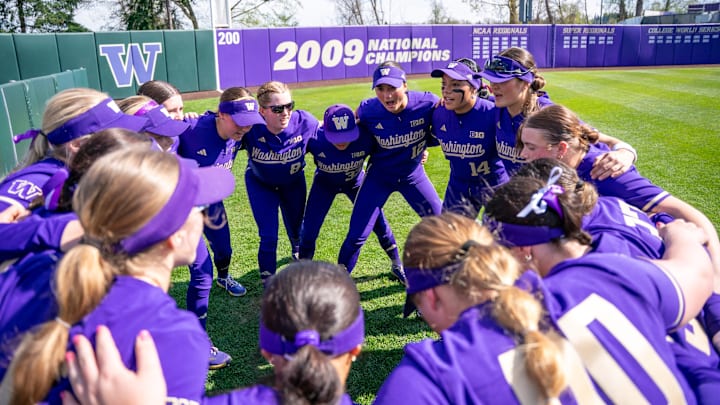The Washington softball team huddles in the outfield before a game.