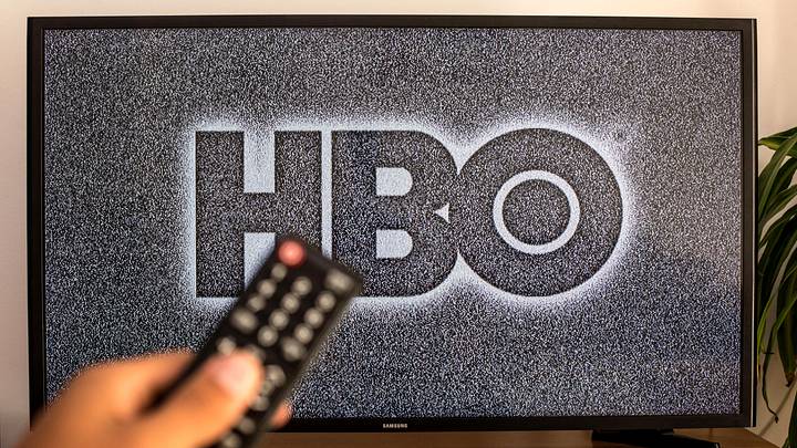 SPAIN – 2021/07/13: In this photo illustration a close-up of a hand holding a TV remote control seen displayed in front of the HBO logo on a tv in the background. (Photo Illustration by Thiago Prudencio/SOPA Images/LightRocket via Getty Images)