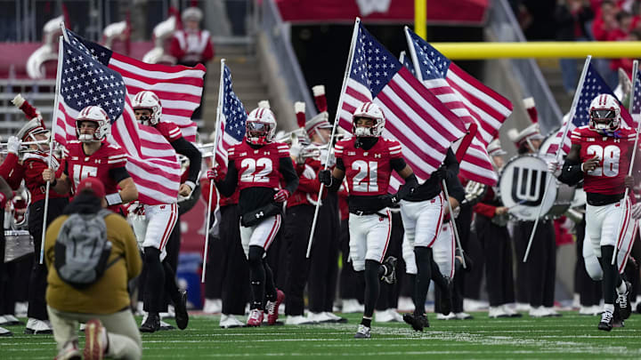 Nov 8, 2025; Madison, Wisconsin, USA;  Wisconsin Badgers players carry American flags while jogging onto the field prior to the game against the Washington Huskies at Camp Randall Stadium. Mandatory Credit: Jeff Hanisch-Imagn Images