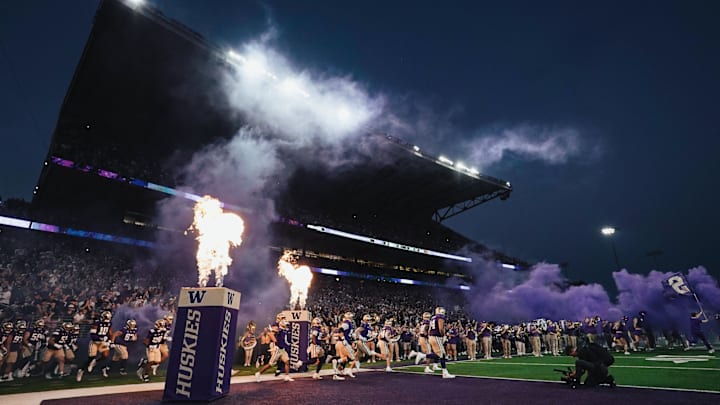 The Huskies take the field for a night game, flames flanking them.