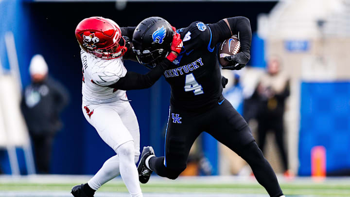 Nov 30, 2024; Lexington, Kentucky, USA; Kentucky Wildcats running back Chip Trayanum (4) is tackled by Louisville Cardinals defensive back Tahveon Nicholson (23) during the fourth quarter at Kroger Field. Mandatory Credit: Jordan Prather-Imagn Images