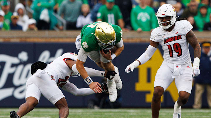 Notre Dame quarterback Riley Leonard, center, flies through the air while being tackled during a NCAA college football game between Notre Dame and Louisville at Notre Dame Stadium on Saturday, Sept. 28, 2024, in South Bend.