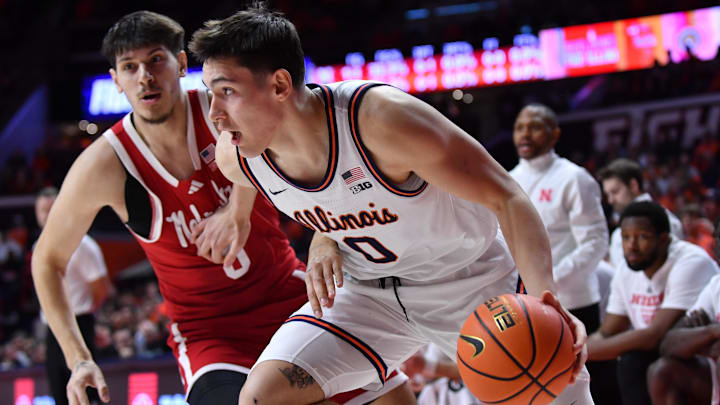 Dec 13, 2025; Champaign, Illinois, USA;  Illinois Fighting Illini forward David Mirkovic (0) drives the ball past Nebraska Cornhuskers forward Berke Buyuktuncel (9) during the first half at State Farm Center. Mandatory Credit: Ron Johnson-Imagn Images