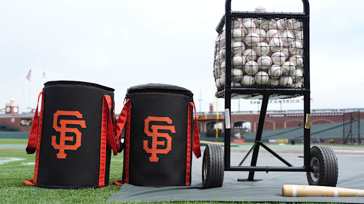 Ball bags with the San Francisco Giants logo sit on the field with a ball cart.