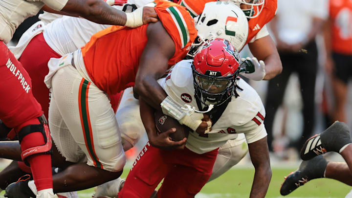Nov 15, 2025; Miami Gardens, Florida, USA; NC State Wolfpack quarterback CJ Bailey (11) is tackled by Miami Hurricanes defensive lineman Armondo Blount (18) during the second quarter at Hard Rock Stadium. Mandatory Credit: Sam Navarro-Imagn Images