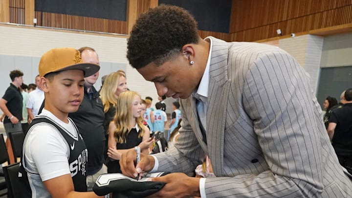 Jun 28, 2025; San Antonio, TX, USA; San Antonio Spurs first round draft pick Carter Bryant signs an autographs for a fan after a press conference at Victory Capital Performance Center. Jun 28, 2025; San Antonio, TX, USA; San Antonio Spurs first round draft pick Carter Bryant signs an autographs for a fan after a press conference at Victory Capital Performance Center.