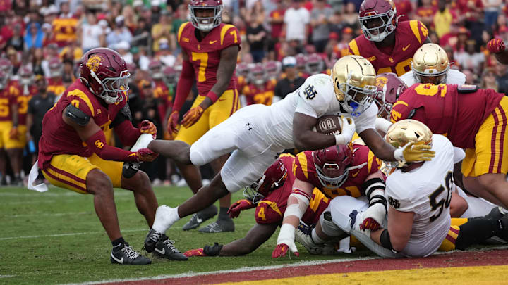 Nov 30, 2024; Los Angeles, California, USA; Notre Dame Fighting Irish running back Jeremiyah Love (4) scores on a 1-yard touchdown run against Southern California Trojans safety Akili Arnold (0) in the first half at United Airlines Field at Los Angeles Memorial Coliseum. Nov 30, 2024; Los Angeles, California, USA; Notre Dame Fighting Irish running back Jeremiyah Love (4) scores on a 1-yard touchdown run against Southern California Trojans safety Akili Arnold (0) in the first half at United Airlines Field at Los Angeles Memorial Coliseum.
