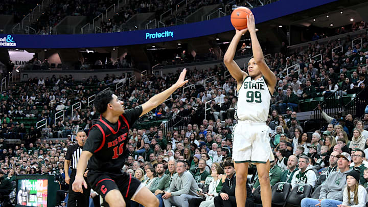 Dec 29, 2025; East Lansing, Michigan, USA;  Michigan State Spartans guard Divine Ugochukwu (99) puts in a three-point shot over Cornell Big Red forward Blake Lecklitner (15) during the second half at Jack Breslin Student Events Center. Mandatory Credit: Dale Young-Imagn Images