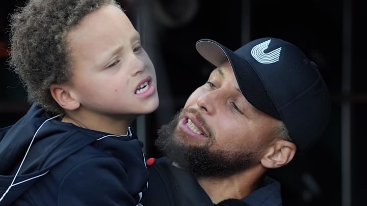 Golden State Warriors guard Stephen Curry (right) holds his son Canon (left) in the San Francisco Giants dugout before the game against the New York Yankees at Oracle Park.