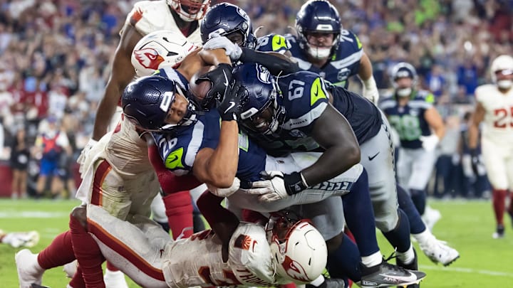 Sep 25, 2025; Glendale, Arizona, USA; Seattle Seahawks running back Zach Charbonnet (26) is pushed across the goal line by tackle Charles Cross (67) to score a touchdown against Arizona Cardinals safety Jalen Thompson (34) in the second quarter at State Farm Stadium. Mandatory Credit: Mark J. Rebilas-Imagn Images