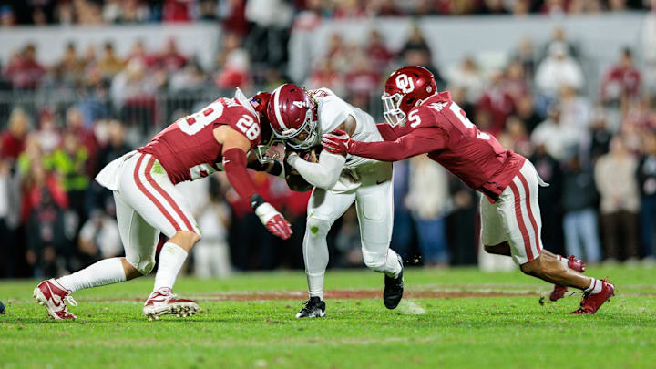 Nov 23, 2024; Norman, Oklahoma, USA; Alabama Crimson Tide quarterback Jalen Milroe (4) is hit by Oklahoma Sooners linebacker Danny Stutsman (28) and defensive back Woodi Washington (5) during the first quarter at Gaylord Family-Oklahoma Memorial Stadium. Mandatory Credit: William Purnell-Imagn Images
