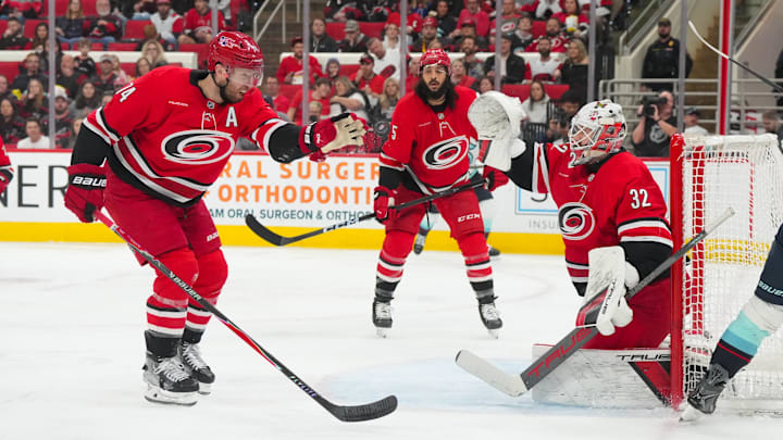 Jan 10, 2026; Raleigh, North Carolina, USA;  Carolina Hurricanes defenseman Jaccob Slavin (74) and Carolina Hurricanes goaltender Brandon Bussi (32) reach for the puck against the Seattle Kraken during the second period at Lenovo Center. Mandatory Credit: James Guillory-Imagn Images
