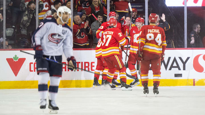 Blue Jackets forward Zach Aston-Reese skates to the bench while the Calgary Flames celebrate their fourth goal of the night.