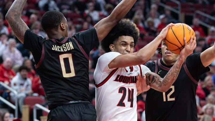 Louisville’s Chucky Hepburn splits Florida State defenders Taylor Bol Bowen, left, and Malique Ewin, right on his way to the basket during a game at the YUM Center. Feb. 22, 2025