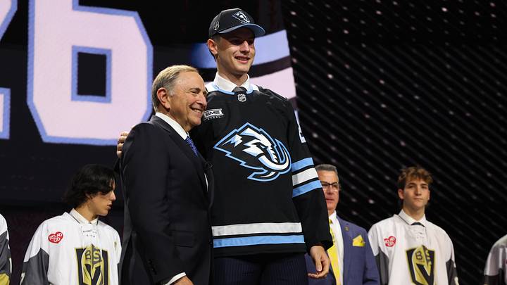 Jun 26, 2026; Buffalo, New York, USA; Ethan Belchetz reacts beside NHL commissioner Gary Bettman after being selected with the seventeenth pick in the first round of the 2026 NHL Draft by the Utah Mammoth at KeyBank Center. Mandatory Credit: Timothy T. Ludwig-Imagn Images