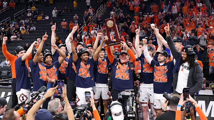 Mar 28, 2026; Houston, TX, USA; Illinois Fighting Illini head coach Brad Underwood celebrates with the trophy on the podium after defeating the Iowa Hawkeyes in an Elite Eight game of the South Regional of the men's 2026 NCAA Tournament at Toyota Center. Mandatory Credit: Troy Taormina-Imagn Images