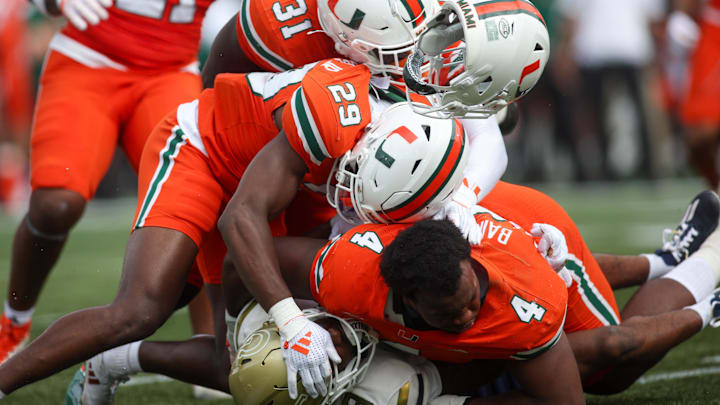 Nov 9, 2024; Atlanta, Georgia, USA; Georgia Tech Yellow Jackets wide receiver Malik Rutherford (8) is tackled by Miami Hurricanes defensive back OJ Frederique Jr. (29) and linebacker Wesley Bissainthe (31) and defensive lineman Rueben Bain Jr. (4) in the second quarter at Bobby Dodd Stadium at Hyundai Field. Mandatory Credit: Brett Davis-Imagn Images
