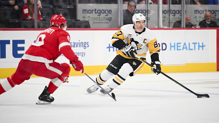 Oct 10, 2024; Detroit, Michigan, USA; Pittsburgh Penguins center Sidney Crosby (87) brings the puck up ice against Detroit Red Wings defenseman Ben Chiarot (8) during the first period at Little Caesars Arena. Mandatory Credit: Tim Fuller-Imagn Images