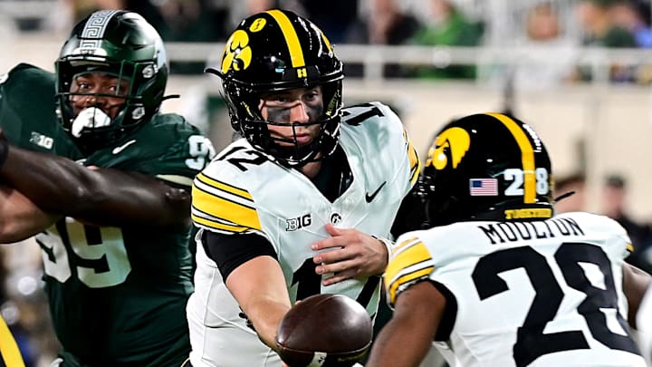 Oct 19, 2024; East Lansing, Michigan, USA;  Iowa Hawkeyes quarterback Cade McNamara (12) hands off to Iowa Hawkeyes running back Kamari Moulton (28) against the Michigan State Spartans at Spartan Stadium. Mandatory Credit: Dale Young-Imagn Images