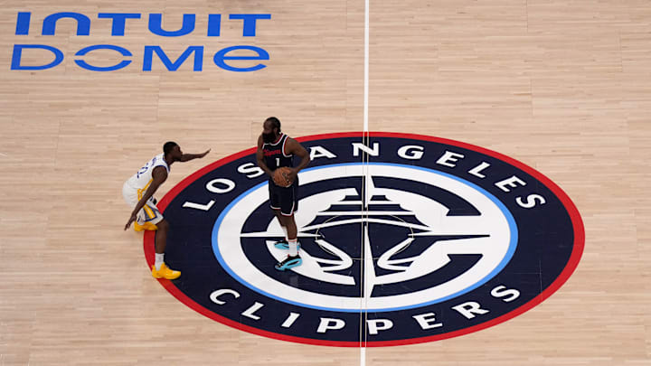 A general view as LA Clippers guard James Harden (1) controls the ball against Golden State Warriors forward Andrew Wiggins (22) on the Clippers logo at midcourt in the first half at Intuit Dome.