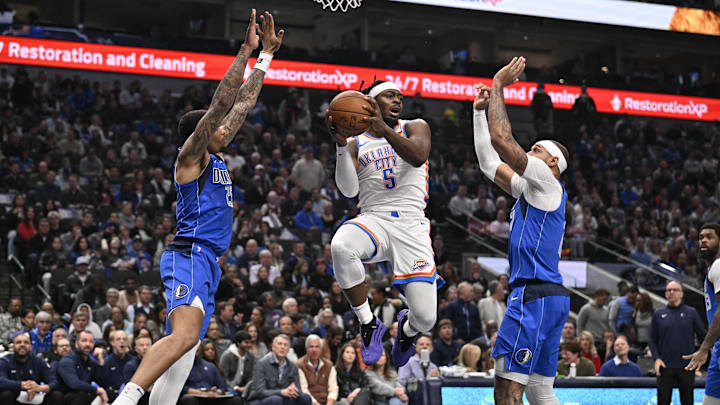 Jan 17, 2025; Dallas, Texas, USA; Oklahoma City Thunder guard Luguentz Dort (5) passes the ball between Dallas Mavericks forward P.J. Washington (25) and center Daniel Gafford (21) during the first quarter at the American Airlines Center. Mandatory Credit: Jerome Miron-Imagn Images Jan 17, 2025; Dallas, Texas, USA; Oklahoma City Thunder guard Luguentz Dort (5) passes the ball between Dallas Mavericks forward P.J. Washington (25) and center Daniel Gafford (21) during the first quarter at the American Airlines Center. Mandatory Credit: Jerome Miron-Imagn Images