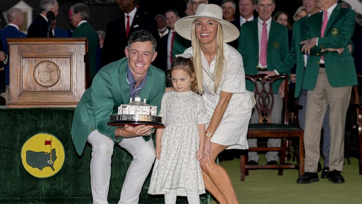Rory McIlroy holds the Masters championship trophy while posing for photographs with his wife, Erica Stoll, and daughter, Poppy, at the green jacket ceremony during the final round of the Masters Tournament at Augusta National Golf Club.